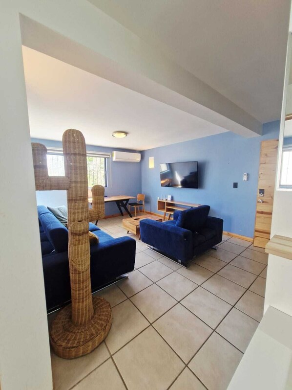 A living room with a blue sofa, a wicker chair, a TV, and a window.