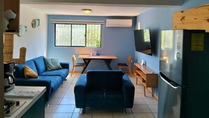 A compact living space with a kitchenette, a dining area, and a TV mounted on the wall. - MARINA AZUL Charming 2-bedroom apartment in beautiful La Paz with WiFi, AC (La Paz BCS)
