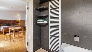 Une salle de bain moderne avec une baignoire blanche, un porte-serviettes et un banc en bois dans la pièce adjacente.