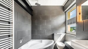 Une salle de bain moderne avec une baignoire sur pieds, des toilettes et une grande fenêtre qui laisse entrer la lumière naturelle.