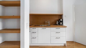 Une cuisine compacte dotée d’un plan de travail en bois, de meubles blancs, d’un évier en acier inoxydable et d’une machine à café.