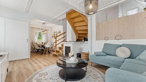 Una sala de estar moderna con un sofá azul, una mesa de centro redonda y una escalera que sube a un nivel superior.