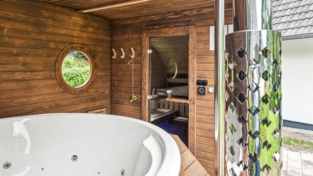 Una cabaña de madera con un jacuzzi, una ventana con vistas a la vegetación y una puerta que da a una zona de cocina.