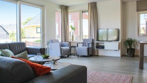 Ein modernes Wohnzimmer mit einer Couch, zwei Sesseln, einem Couchtisch, einem Fernseher und einem kleinen Beistelltisch.