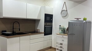 A modern kitchen with white cabinets, a stainless steel sink, a microwave, an oven, and a grey refrigerator.