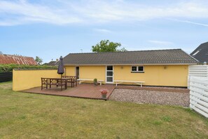 A yellow building with a tiled roof, a wooden deck, and a white fence. - Apartment in Snogebæk near the beach (Nexø)