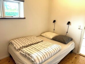 A single bed with a patterned blanket, two pillows, a bedside lamp, and a window with a view of greenery. - Apartment in Snogebæk near the beach (Nexø)