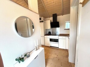 A compact kitchen with white cabinets, a stainless steel range hood, and a round mirror on the wall. - Apartment in Snogebæk near the beach (Nexø)