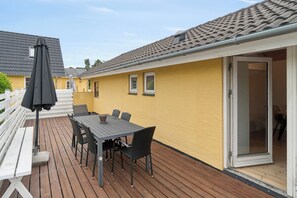 Eine Terrasse im Freien mit Tisch und Stühlen, einer weißen Bank und einer Glasschiebetür.