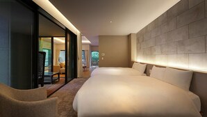 Een moderne hotelkamer met een groot bed, een zithoek met een stoel en uitzicht buiten door een glazen deur.