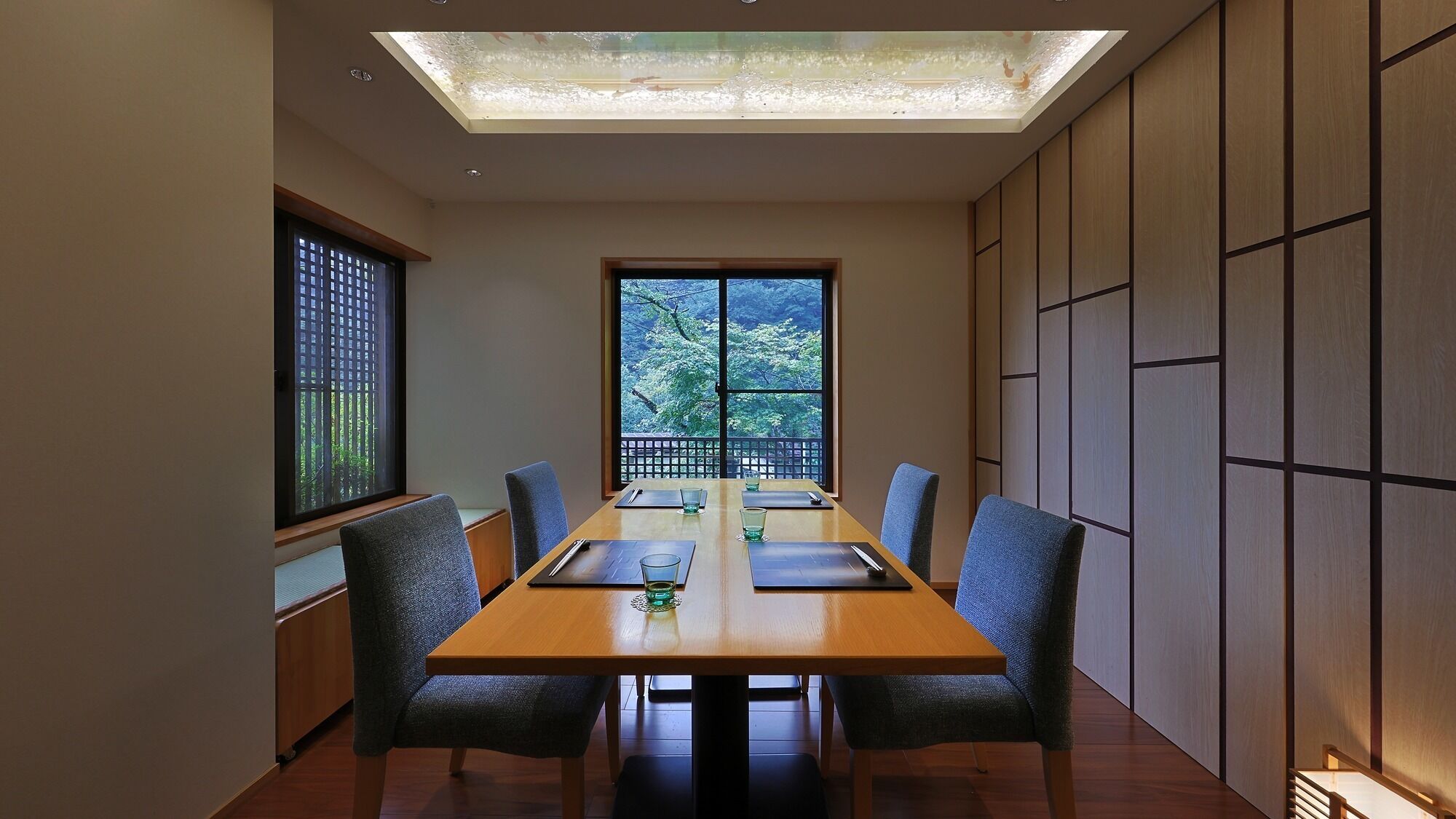 A conference room with a long table, six chairs, and a large window offering a view of trees.