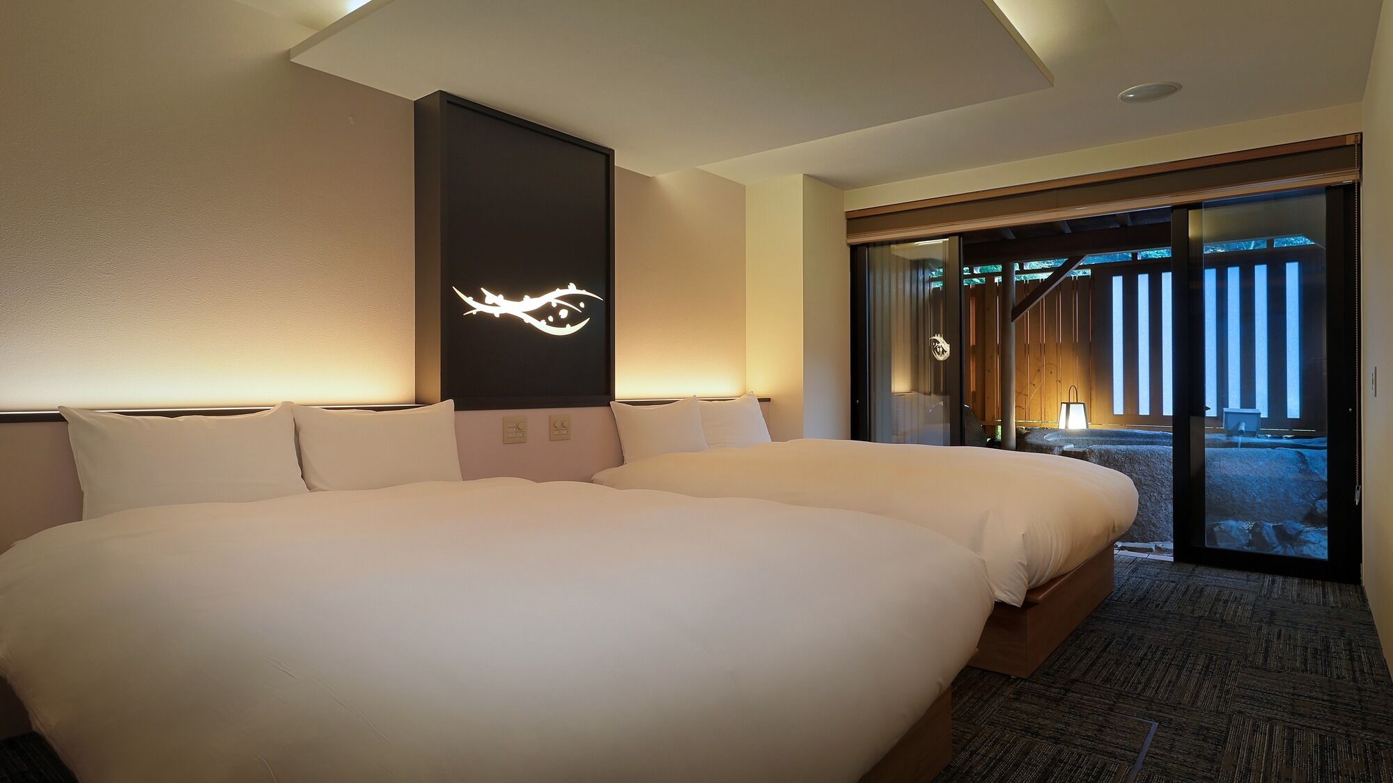 A hotel room with a large bed, a wall-mounted light fixture, and a sliding glass door leading to an outdoor area.