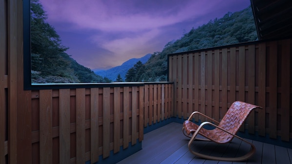 A wooden deck with a rocking chair, a large window overlooking a forested valley, and a wooden fence. - SHIMAONSEN TSURUYA (Nakanojo)