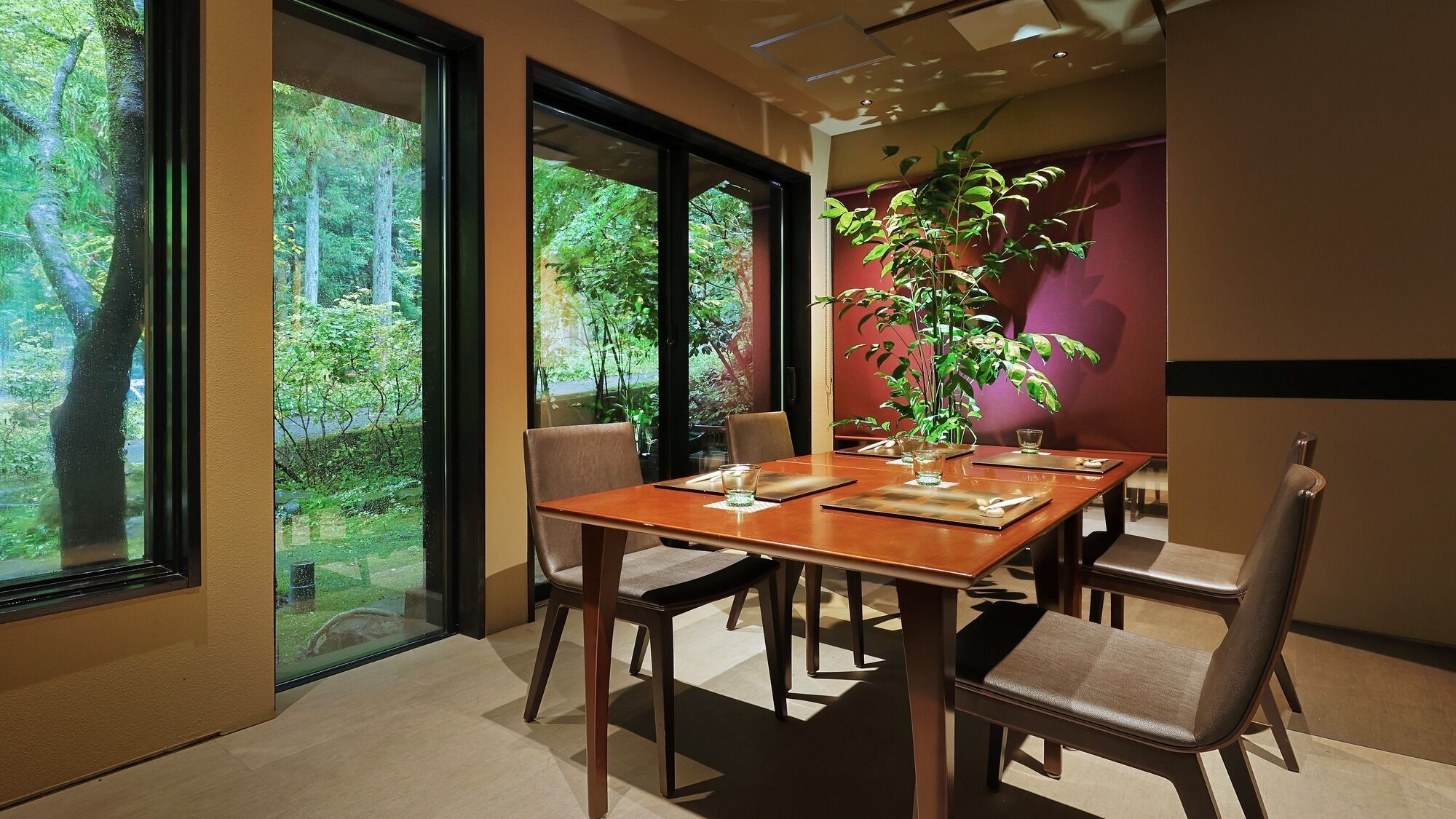 A dining area with a wooden table, four chairs, and a large window offering a view of trees.
