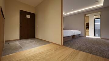 Habitación de hotel con piso de madera, cama con ropa blanca, un escritorio pequeño y una puerta corredera que da a un baño.