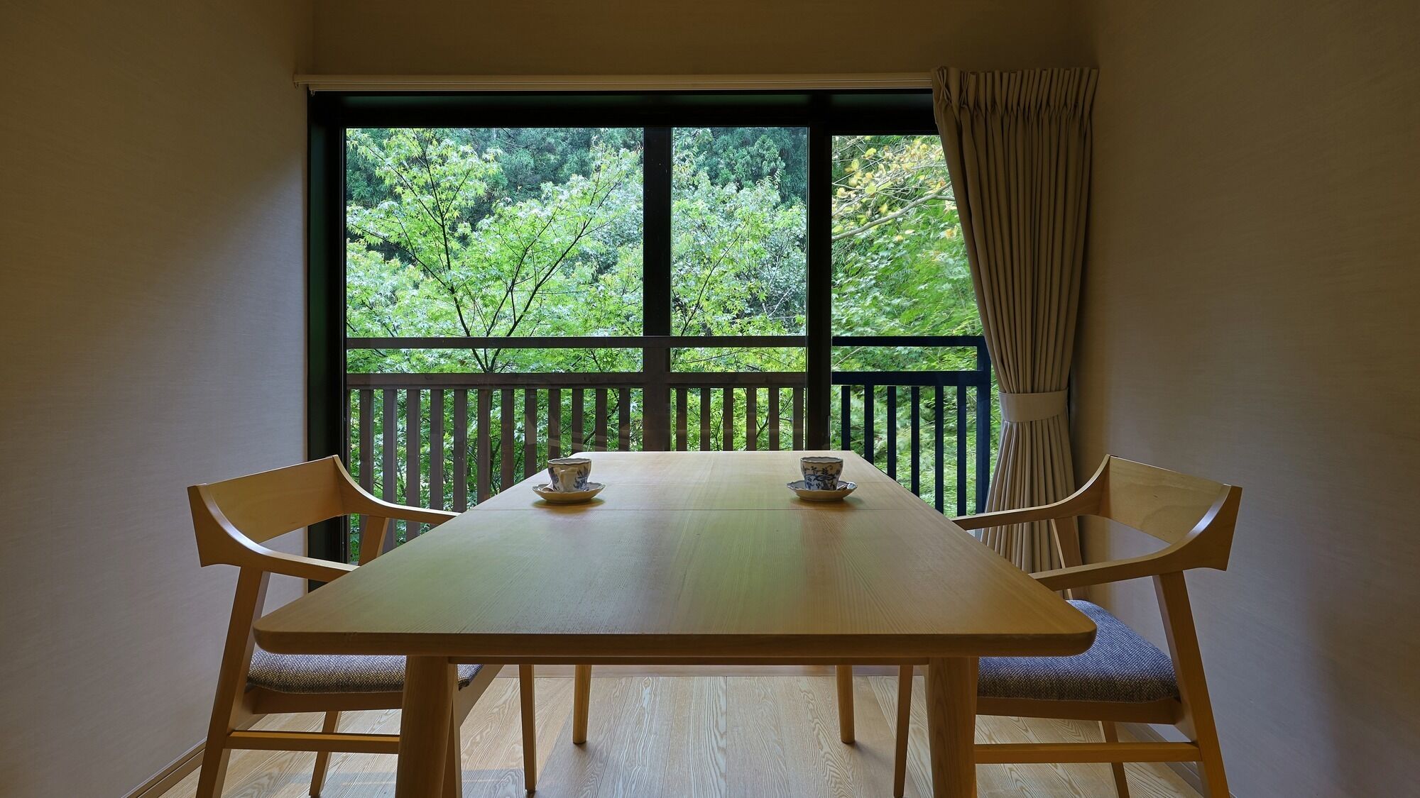 Una habitación con una mesa y sillas de madera, una ventana con vistas a árboles y una cortina.