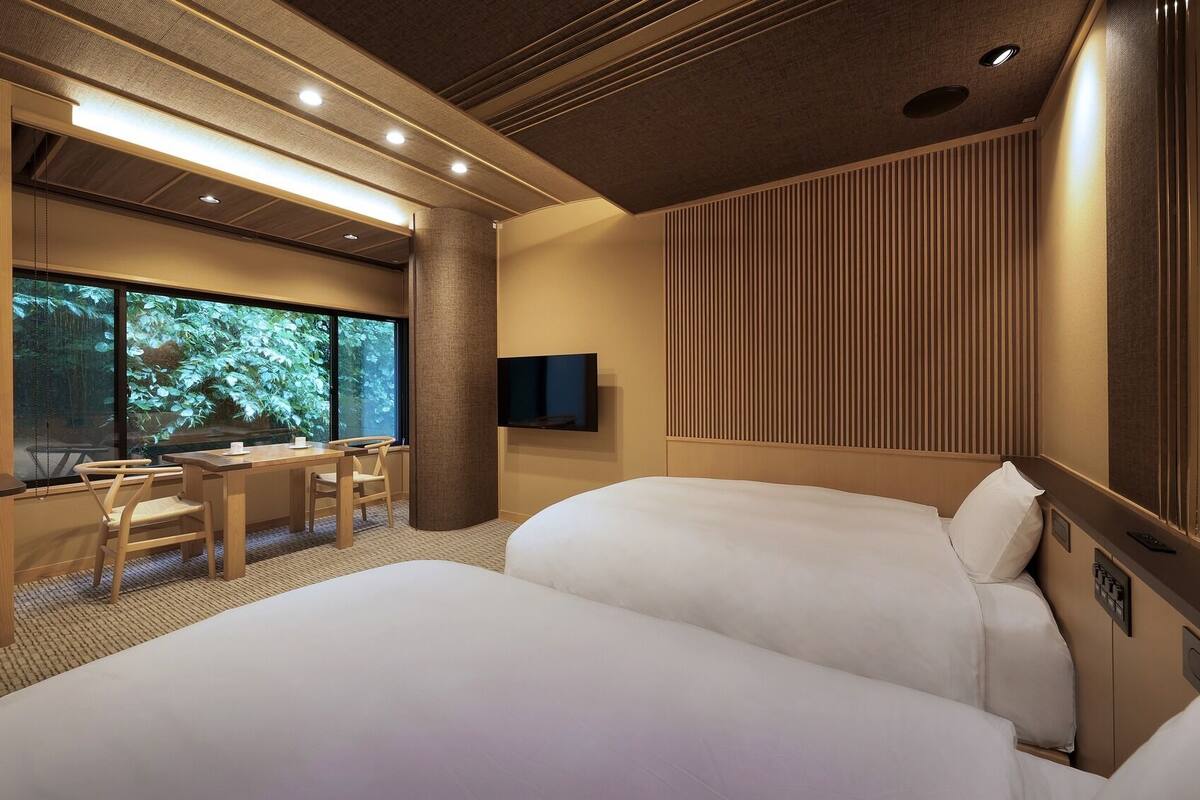 Ein Hotelzimmer mit einem großen Bett, einem Schreibtisch mit Stühlen, einem Fernseher und einem Fenster mit Blick auf Grünflächen.