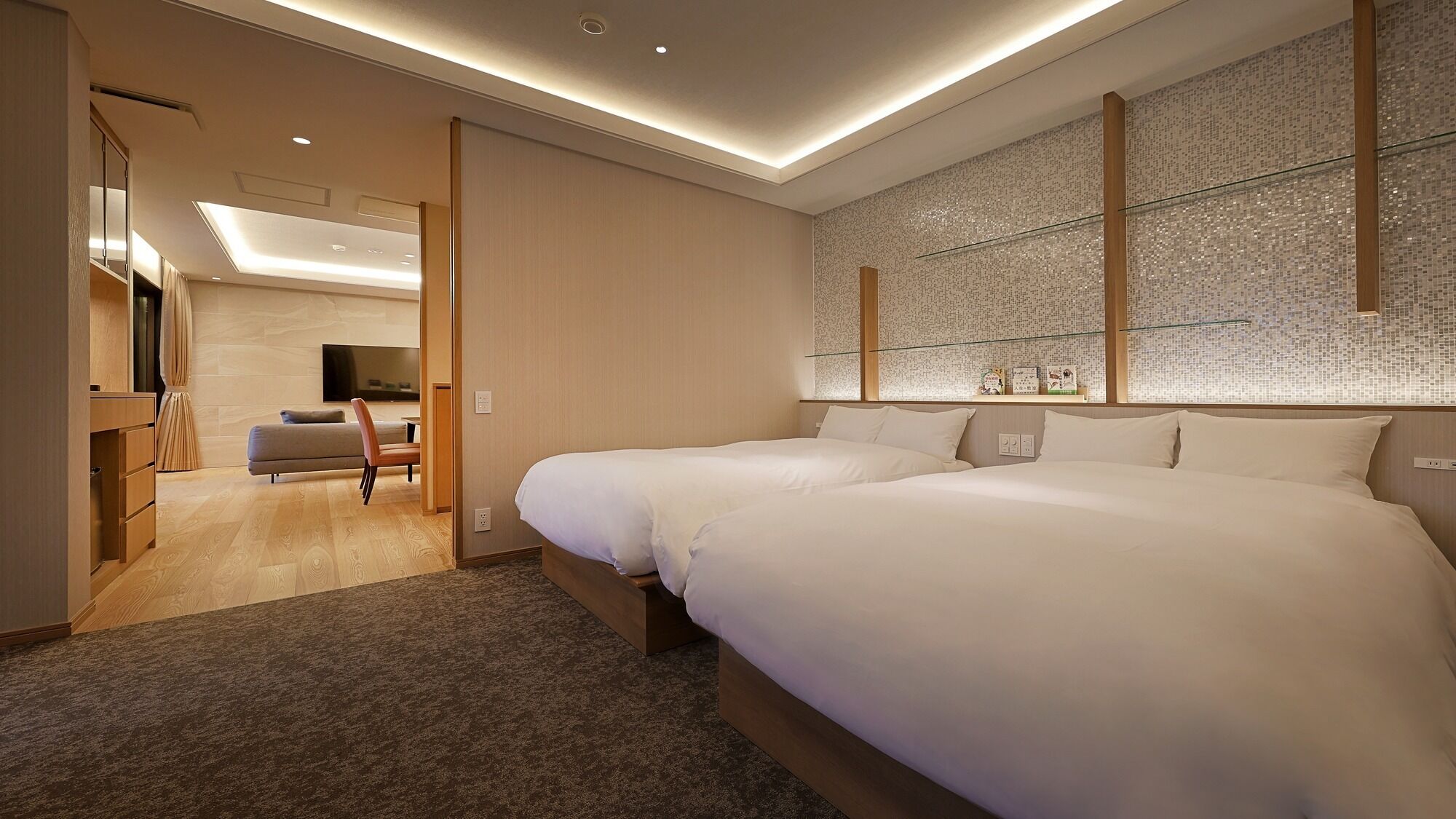 A modern hotel room with a large bed, a seating area with a sofa and chairs, and a decorative wall with a mosaic pattern.