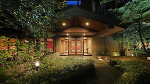 Een traditioneel Japans gebouw met een houten entree, omringd door weelderige begroeiing en verlicht met zacht licht.