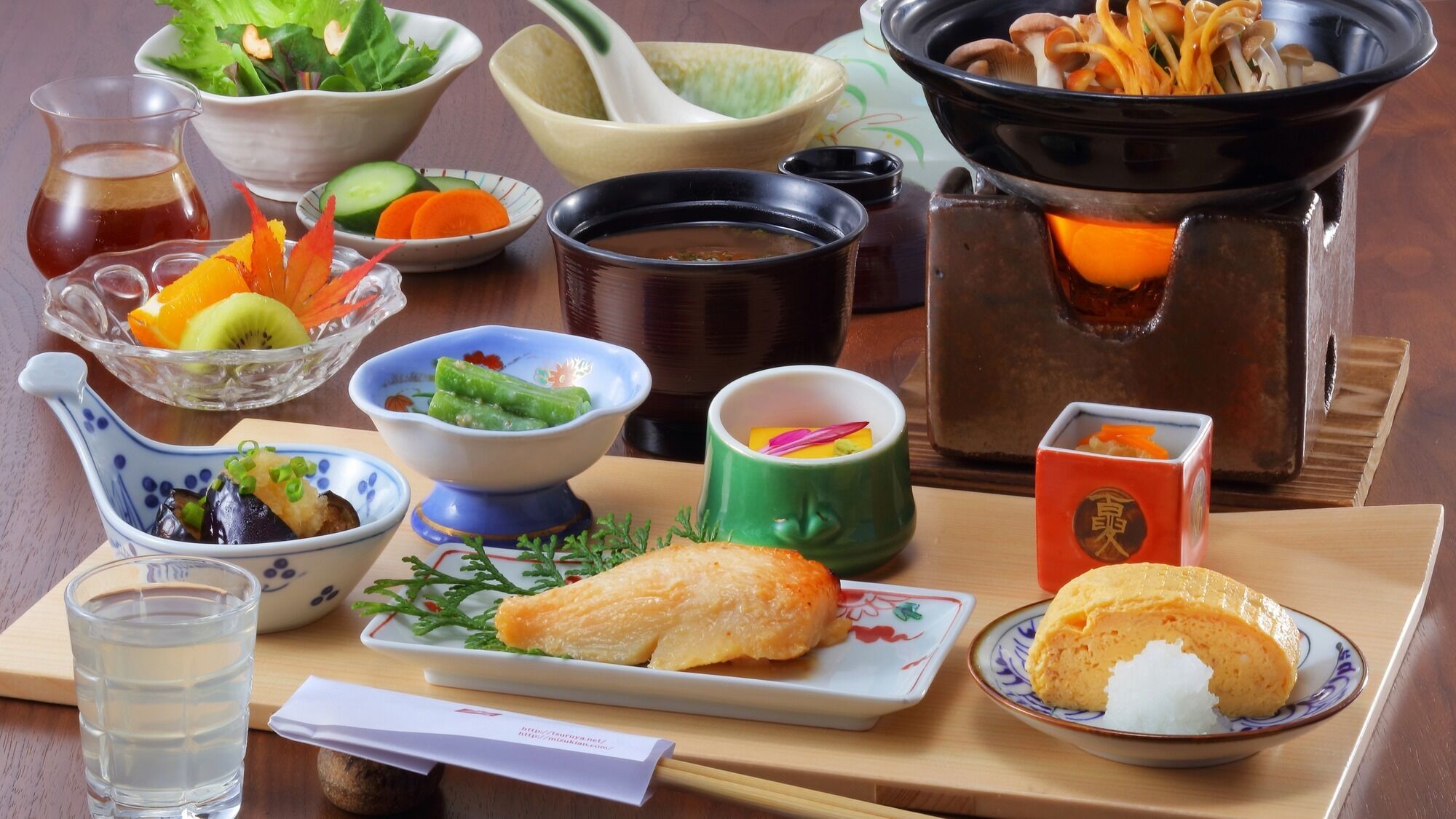 A traditional Japanese meal setup with various dishes, including a hot pot, sashimi, and pickled vegetables.