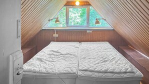 Une pièce avec un plafond en pente et une fenêtre agrémentée de deux lampes. On y trouve deux lits avec du linge de lit blanc.