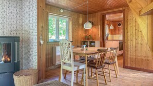 L’intérieur d’un chalet accueillant, avec un coin repas, des murs en bois, une cheminée et une cuisine visible à travers une porte ouverte.