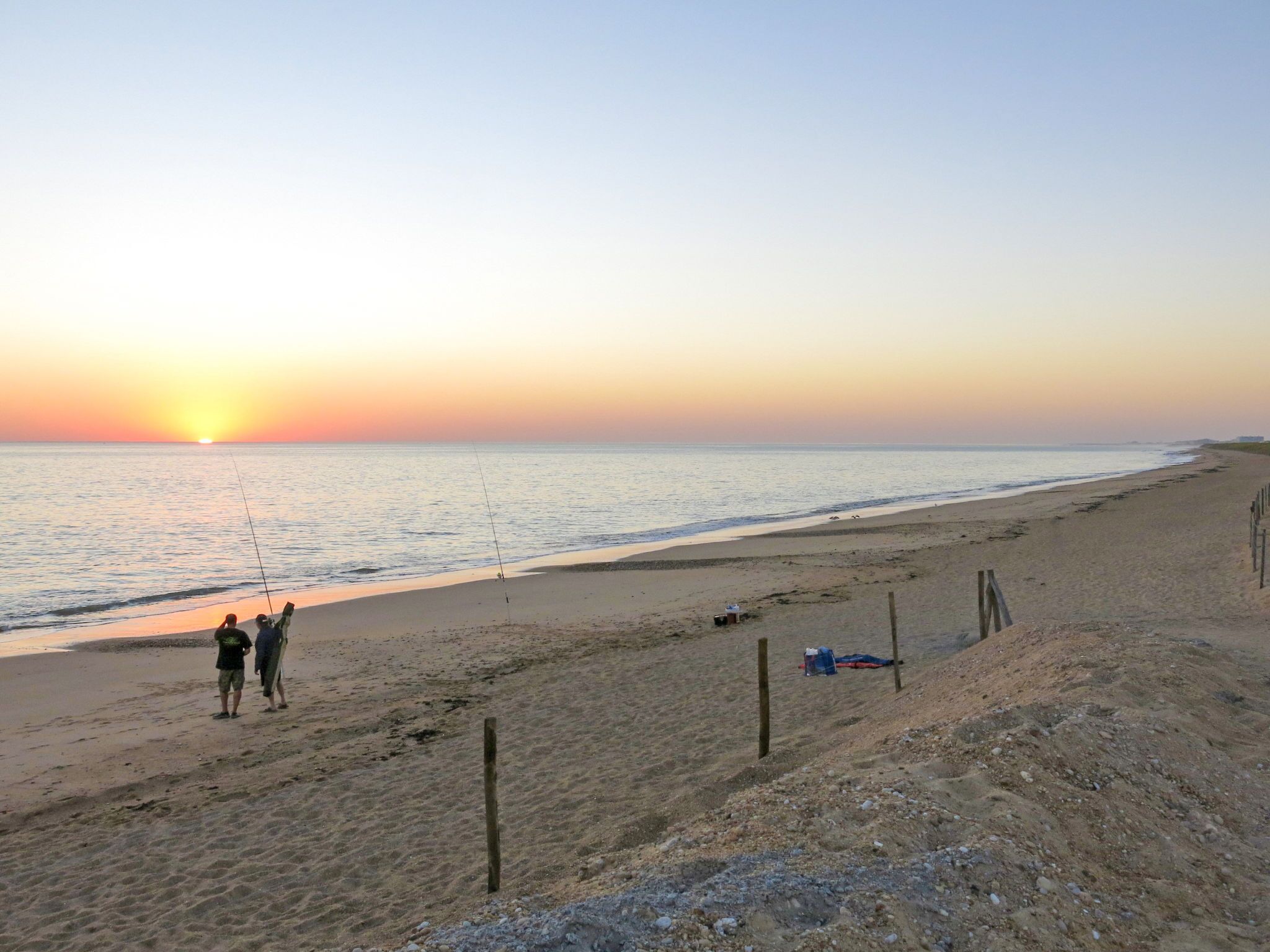 Een strand met een zonsondergang, een vishengel en een paar mensen.