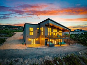 A modern two-story house with a balcony, a hot tub, and a driveway. - Chukar Retreat | Sleeps 24, Ideal Beach Access, Hot Tub, EV! (Garden City)