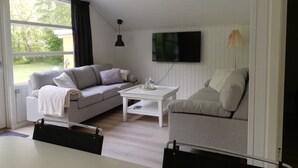 Una sala de estar con un sofá, una silla, una mesa de centro, un televisor y un ventanal con vistas a zonas verdes.