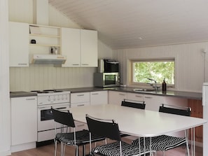 A modern kitchen with white cabinetry, a stove, a microwave, and a window with a view of greenery.