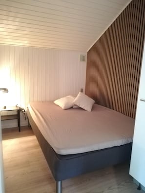 A single bed with a mattress and pillows, a bedside table with a lamp, and a wooden slat wall.