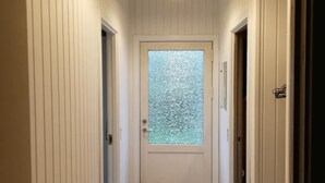 Un pasillo con una puerta blanca, un ventanal con vidrio texturizado y un felpudo negro.