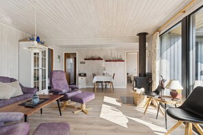 A modern living room with a sofa, chairs, a dining table, and a fireplace. - Lovely cottage close to the water (Hadsund)
