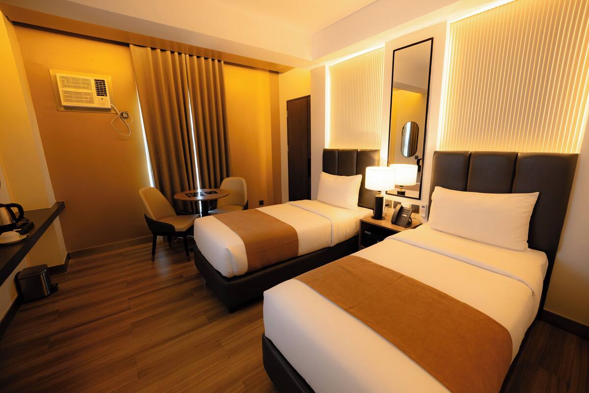 Ett hotellrum med två sängar, ett skrivbord, en stol, en lampa, en telefon och en spegel.