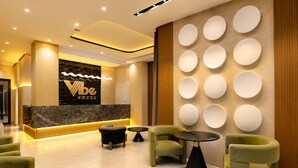 Un espace d’accueil d’hôtel avec un comptoir en marbre, des fauteuils à revêtement vert et un mur orné d’appliques lumineuses rondes.