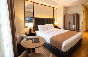 A hotel room with a bed, bedside tables, a desk, a chair, a round table, and a wardrobe. - Vibe Hotel Alabang (Muntinlupa)