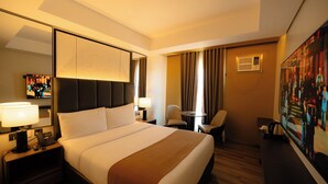 Ein Hotelzimmer mit einem großen Bett, einem Schreibtisch, einem Sessel, einem Fernseher und einem Bild an der Wand.