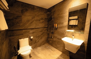 A modern bathroom with a toilet, shower, and sink, all against a dark marble wall.