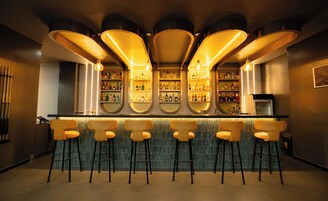 A bar area with multiple stools, shelves of bottles, and a counter.