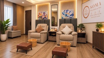 A modern spa room with two reclining chairs, a massage table, and a reception desk.