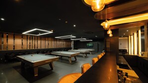 Ein Billardbereich mit mehreren Tischen, einer Bar mit Hockern und Deckenleuchten.