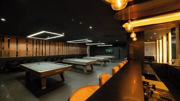 A pool table area with multiple tables, a bar with stools, and overhead lighting fixtures.