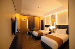 A hotel room with two beds, a desk, a chair, a TV, and a mirror.