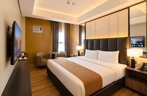A hotel room with a large bed, a desk, a chair, a TV, and a mirror. - Vibe Hotel Alabang (Muntinlupa)