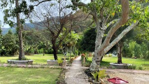 A pathway in a park with trees and a small white structure with a red roof. - Roman Sinasi Hotel (Merek)