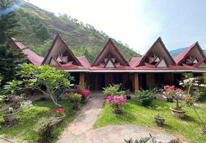 A row of triangular-roofed buildings with a garden in front. - Roman Sinasi Hotel (Merek)