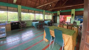 A spacious indoor area with tables and chairs, a refrigerator, and a television. - Roman Sinasi Hotel (Merek)