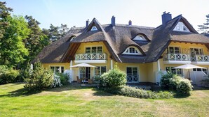 A two-story house with a thatched roof, large windows, and a balcony with a white railing.