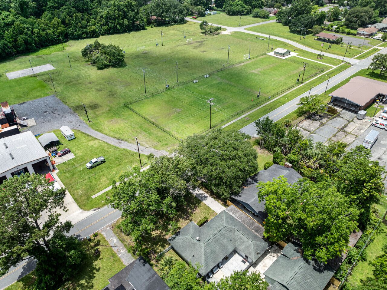 An aerial view of a residential area with a large green field, houses, and a road.