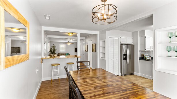 A modern kitchen with a wooden dining table, white cabinets, and a stainless steel refrigerator.